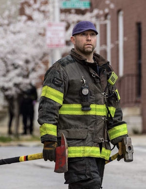 Fireman wearing a Boston Scally Cap while holding an Axe and a Sledge Hammer