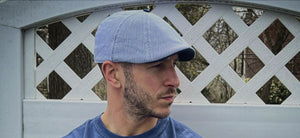 The Derby Cap is back, photo showing man wearing blue and white striped seersucker cap standing in front of white fence