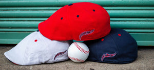 The Youk Cap is here, photo showing the three colorways of the Youk (Red, Navy and a very light grey) stacked on top of each other in front of a green background