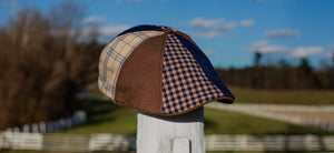 The Triple Crown is here, featuring a patchwork of navy blue, brown and plaids. Cap shown sitting on a fence rail with outdoor scenery behind