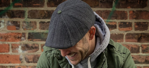 Green Friday Sale 20% off with Code GREENFRIDAY, photo featuring man sitting against brick wall wearing herringbone scally cap and a green jacket